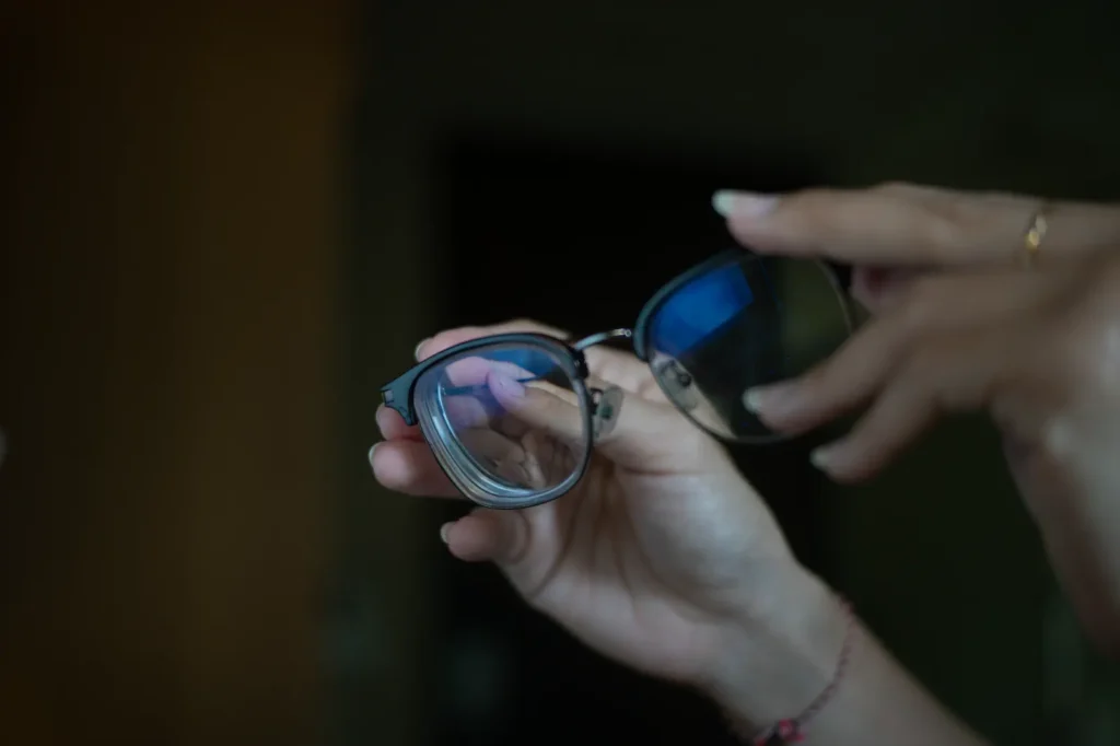 Mano sosteniendo lentes con filtro azul en ambiente interior.