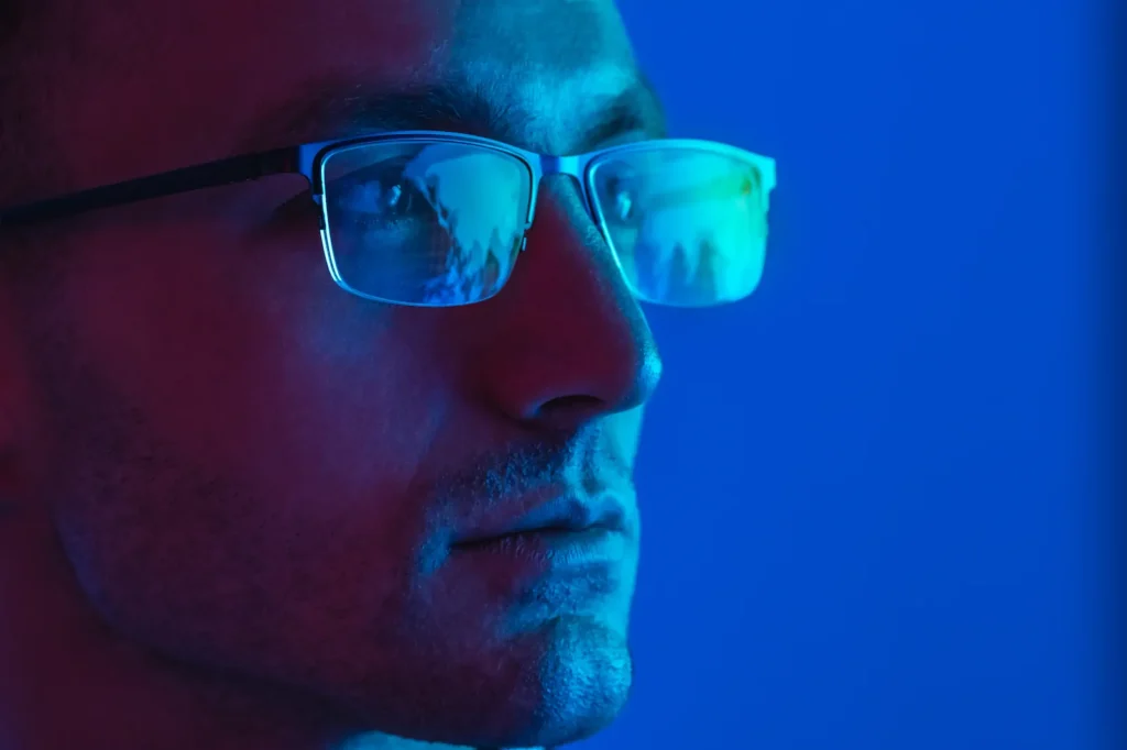 Hombre con lentes con filtro azul mirando una pantalla iluminada.