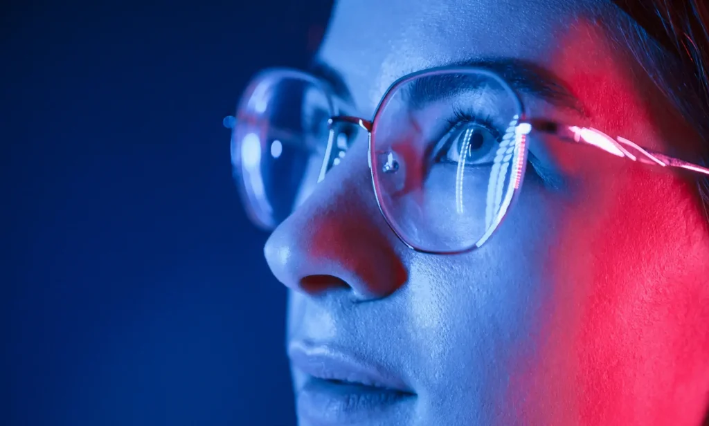 Primer plano de mujer usando lentes con filtro azul bajo luz azul y roja.
