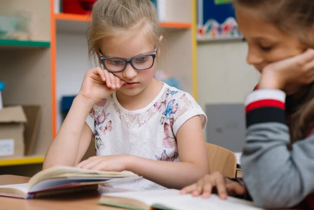 Niña con lentes revisando su tarea con expresión de cansancio.