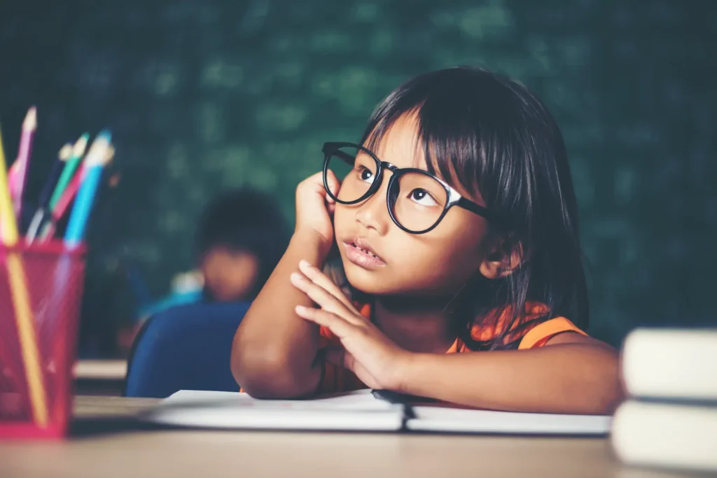Niña con gafas apoyada en el escritorio mirando al frente.