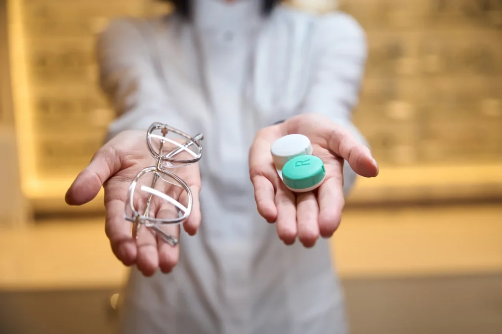Profesional de la salud mostrando en sus manos unos lentes de armazón y un estuche verde para lentes de contacto.