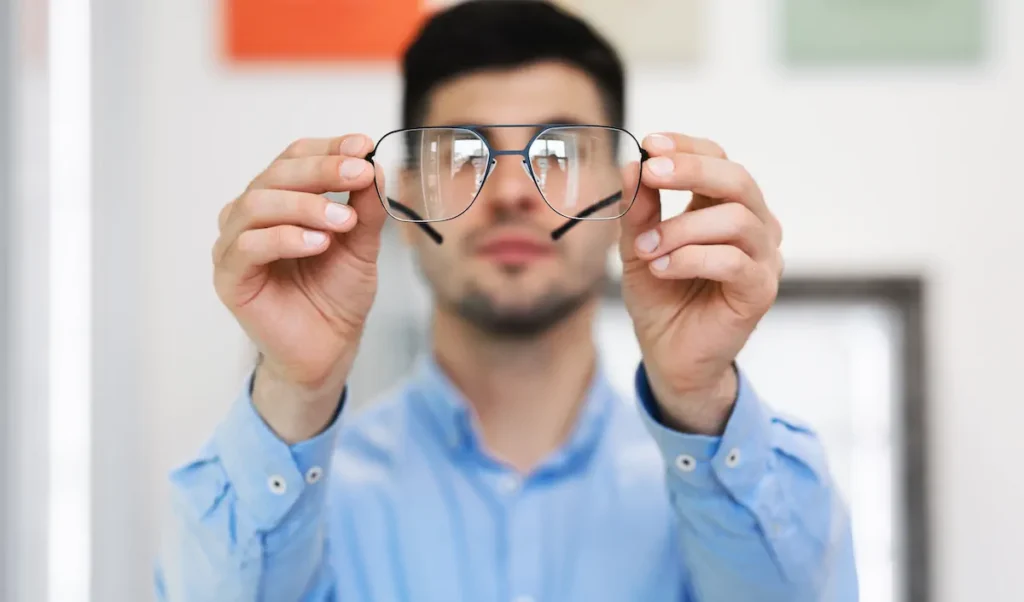 Hombre sosteniendo un par de lentes frente a sí para revisarlos cuidadosamente.