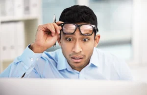 Empleado sorprendido mirando su pantalla mientras ajusta sus gafas.