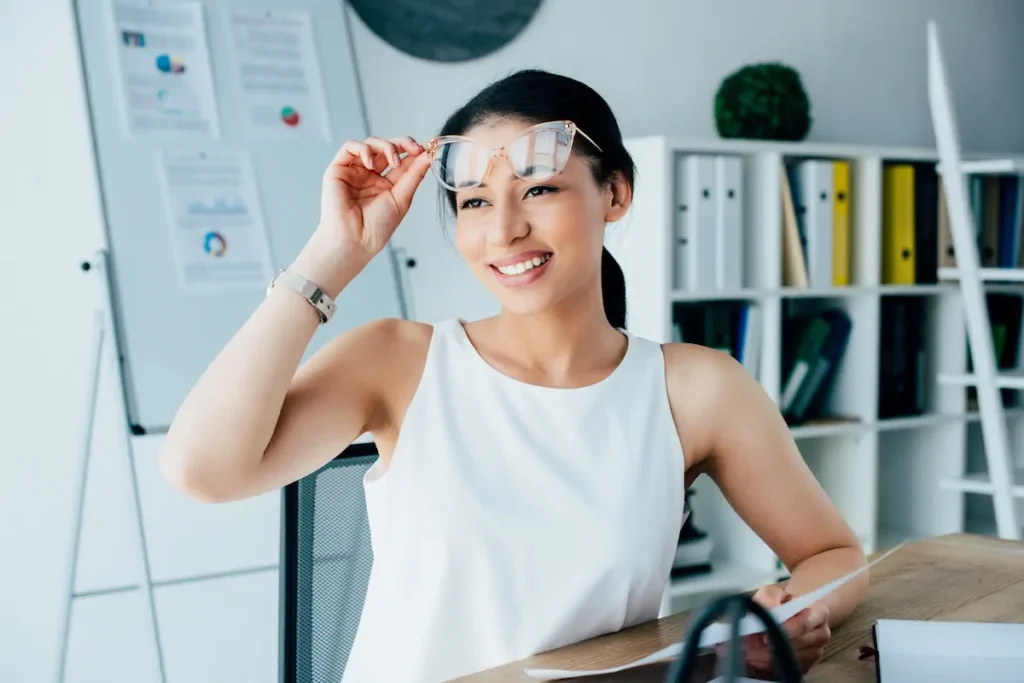 Mujer sonriente probándose unos lentes en su lugar de trabajo.