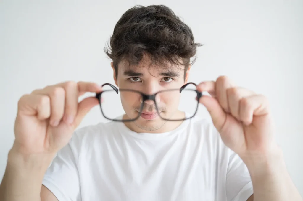 Joven inspeccionando sus gafas de cerca para detectar rayas o cambio de graduación.