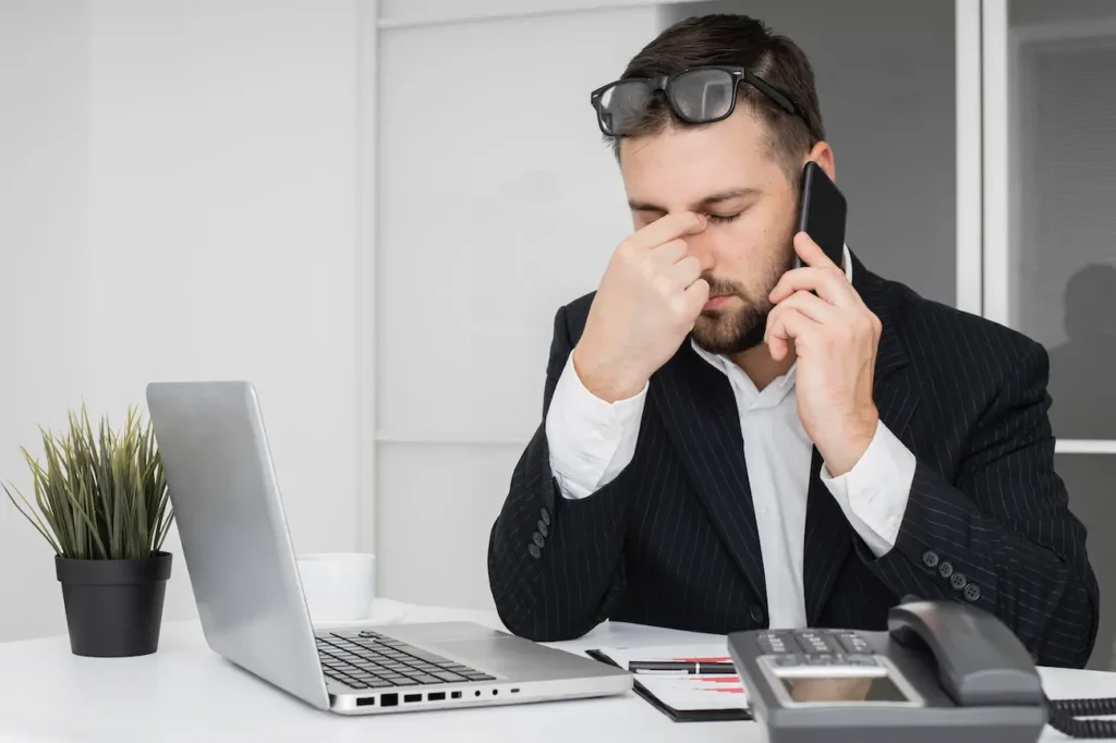 Ejecutivo en oficina tocándose el puente de la nariz por dolor ocular y pantallas; posible necesidad de lentes.