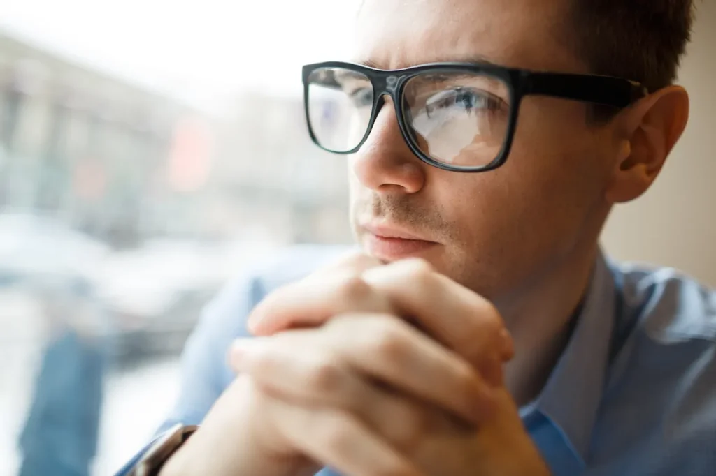 Hombre con gafas mirando a lo lejos, pensando; visión borrosa como síntoma.
