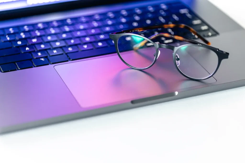Lentes colocados sobre un teclado iluminado, representando el impacto de las pantallas en la salud visual.