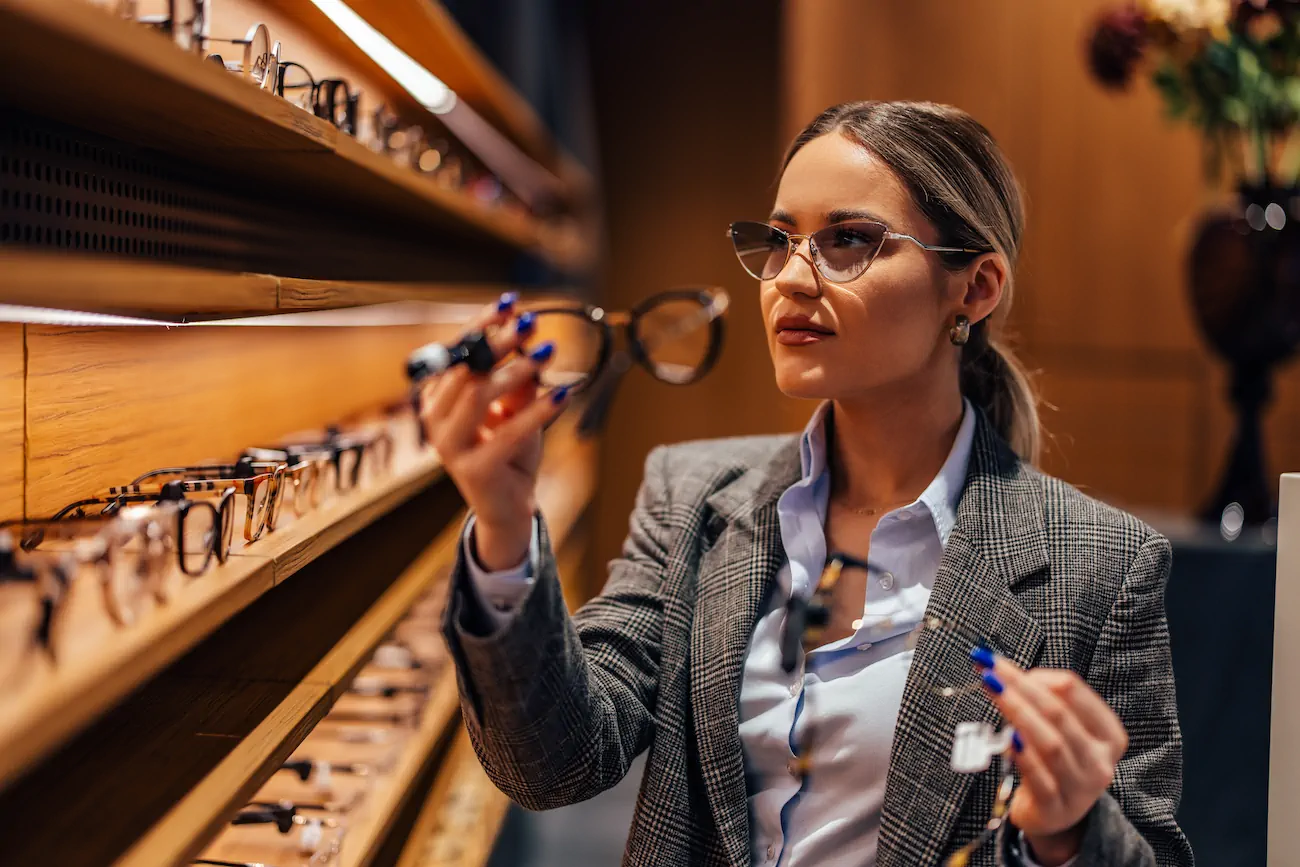 Mujer eligiendo lentes en un estante de óptica.
