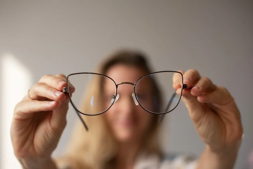 Mujer sosteniendo unos lentes frente a ella mostrando visión borrosa causada por astigmatismo.