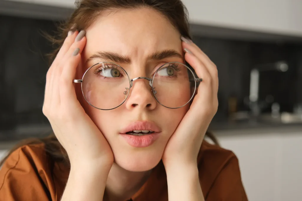 Mujer ajustando sus lentes con expresión de molestia por visión distorsionada típica del astigmatismo.