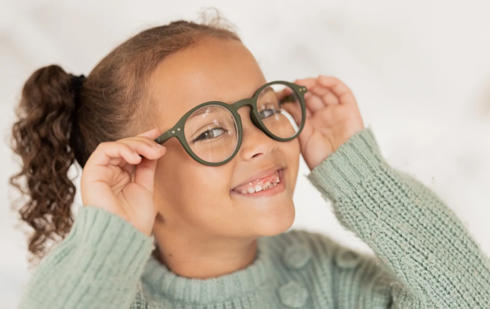 Niña sonriente usando lentes graduados después de examen visual infantil.