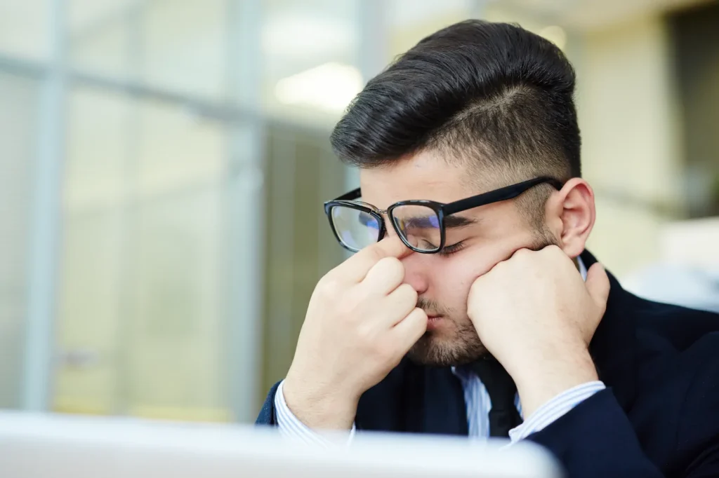 Estudiante con gafas apoyando la cabeza por cansancio ocular tras largas horas en pantalla.