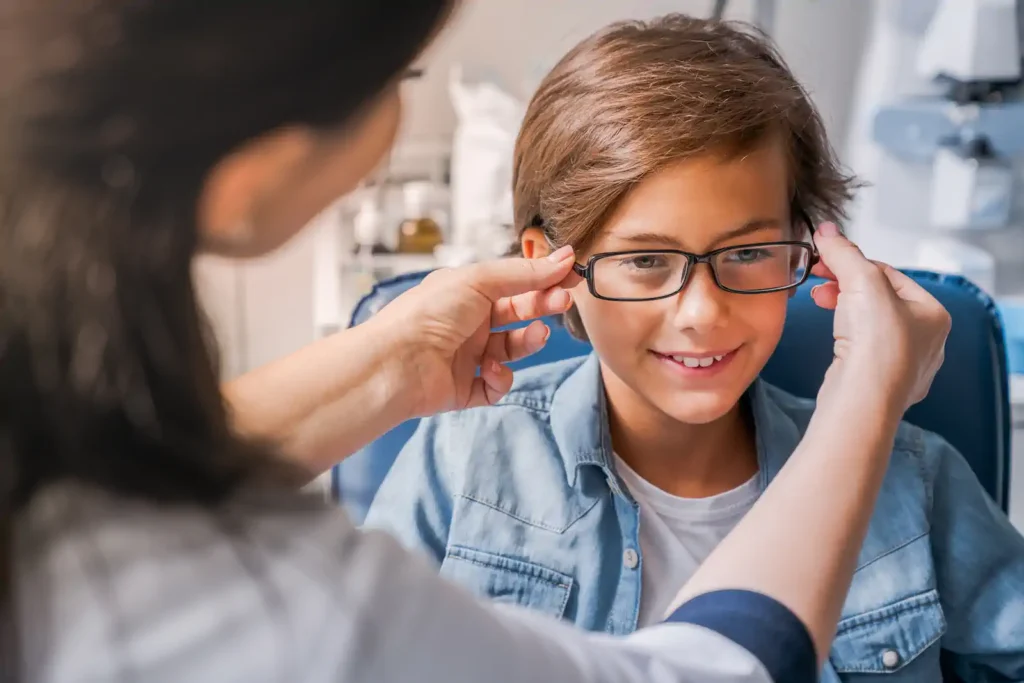 Niño probándose lentes durante su primer examen de la vista con ayuda profesional