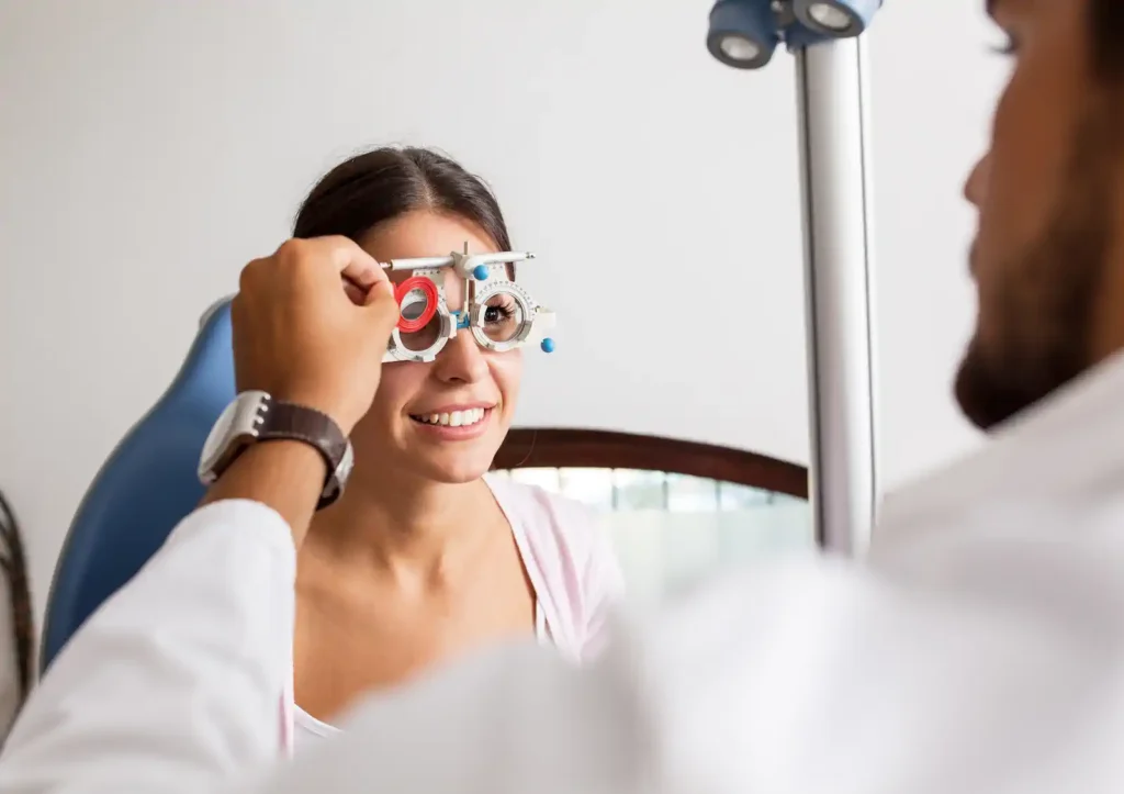 Paciente sonriente realizándose un examen de la vista con foróptero en consulta optométrica