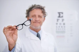 Optometrista sosteniendo gafas frente a tabla optométrica de Snellen para examen visual