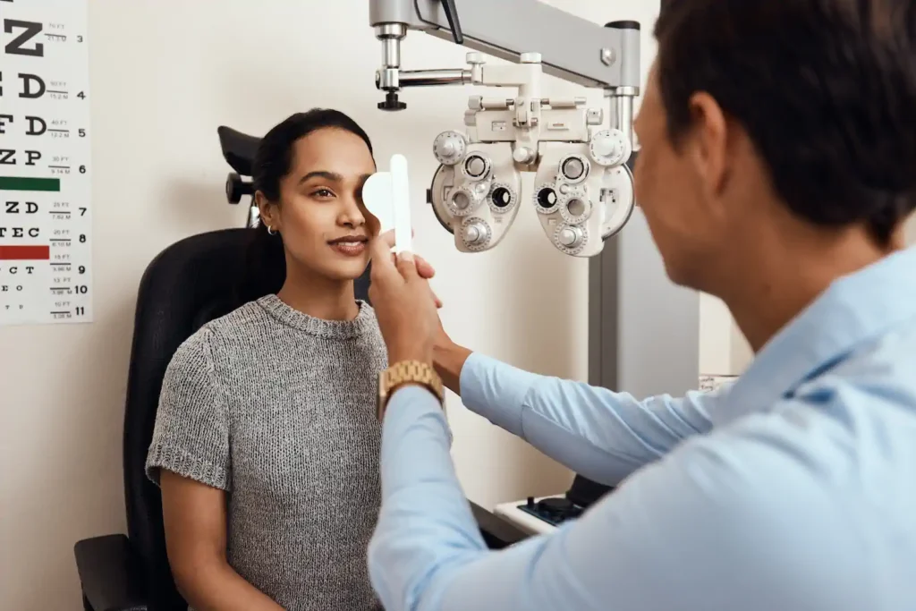 Mujer joven durante examen de la vista con foróptero realizado por optometrista