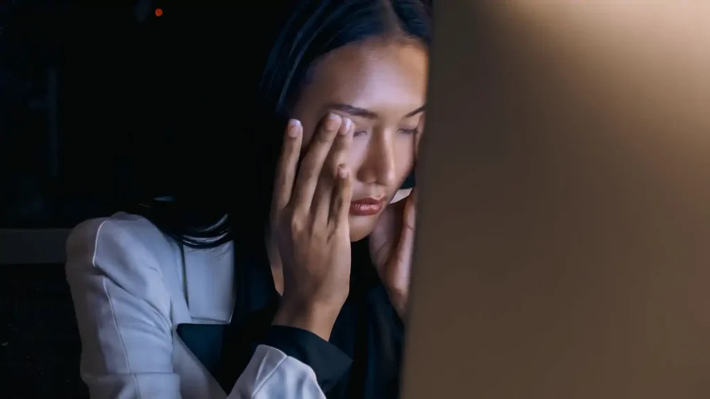 Mujer con fatiga ocular tocándose el rostro tras largas horas frente a la computadora